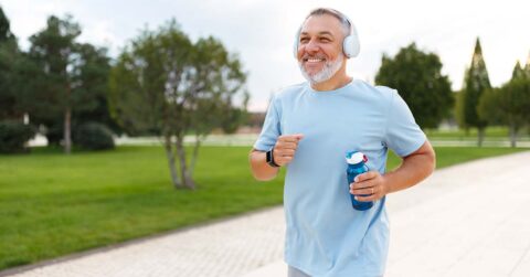 Happy,Mature,Man,In,Headphones,Holding,Water,Bottle,While,Jogging